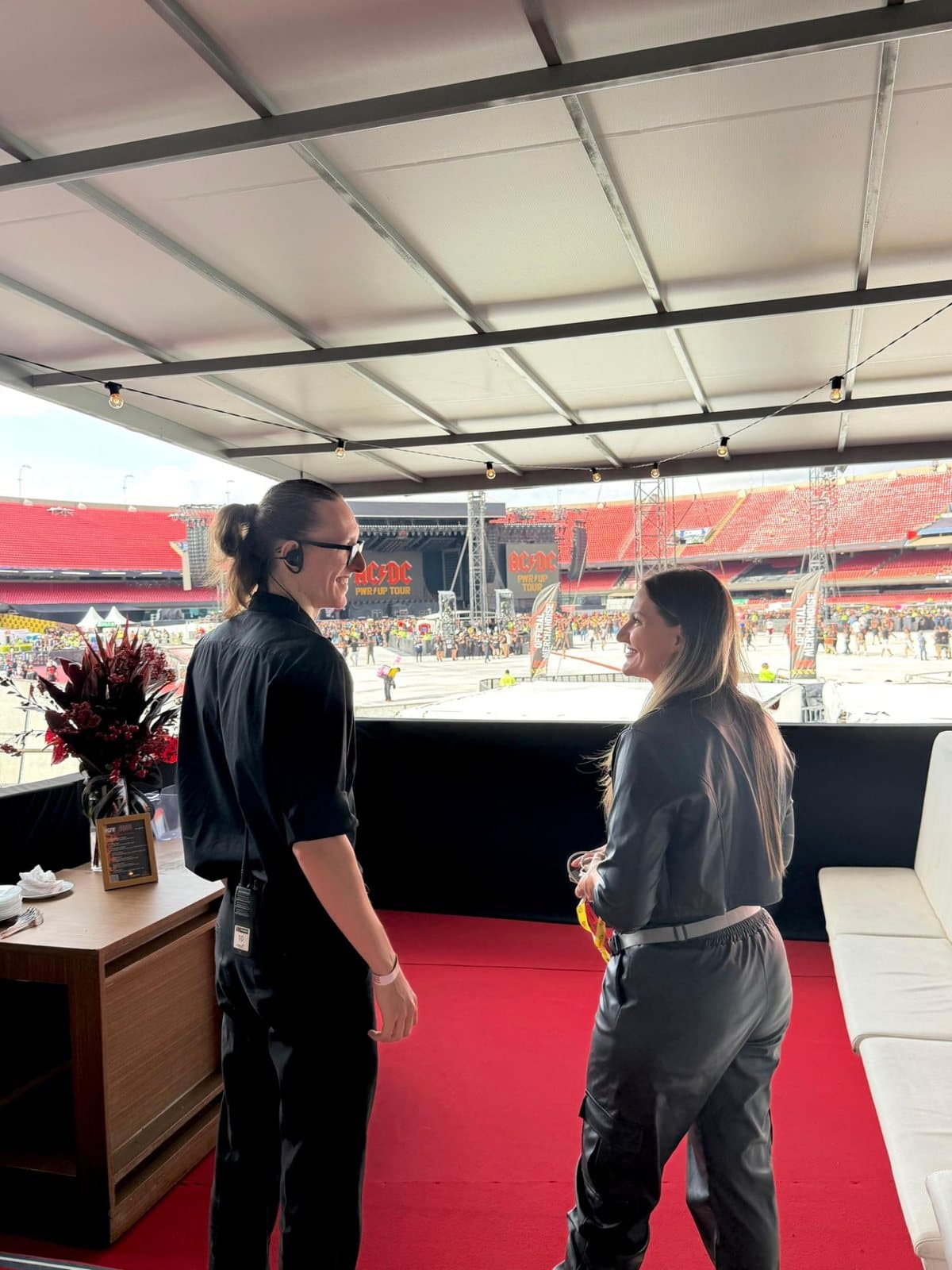 Vinícius e Marcieli Zanatta conversando dentro de um camarote produzido pela Zanatta, com vista para o palco montado no gramado do estádio.